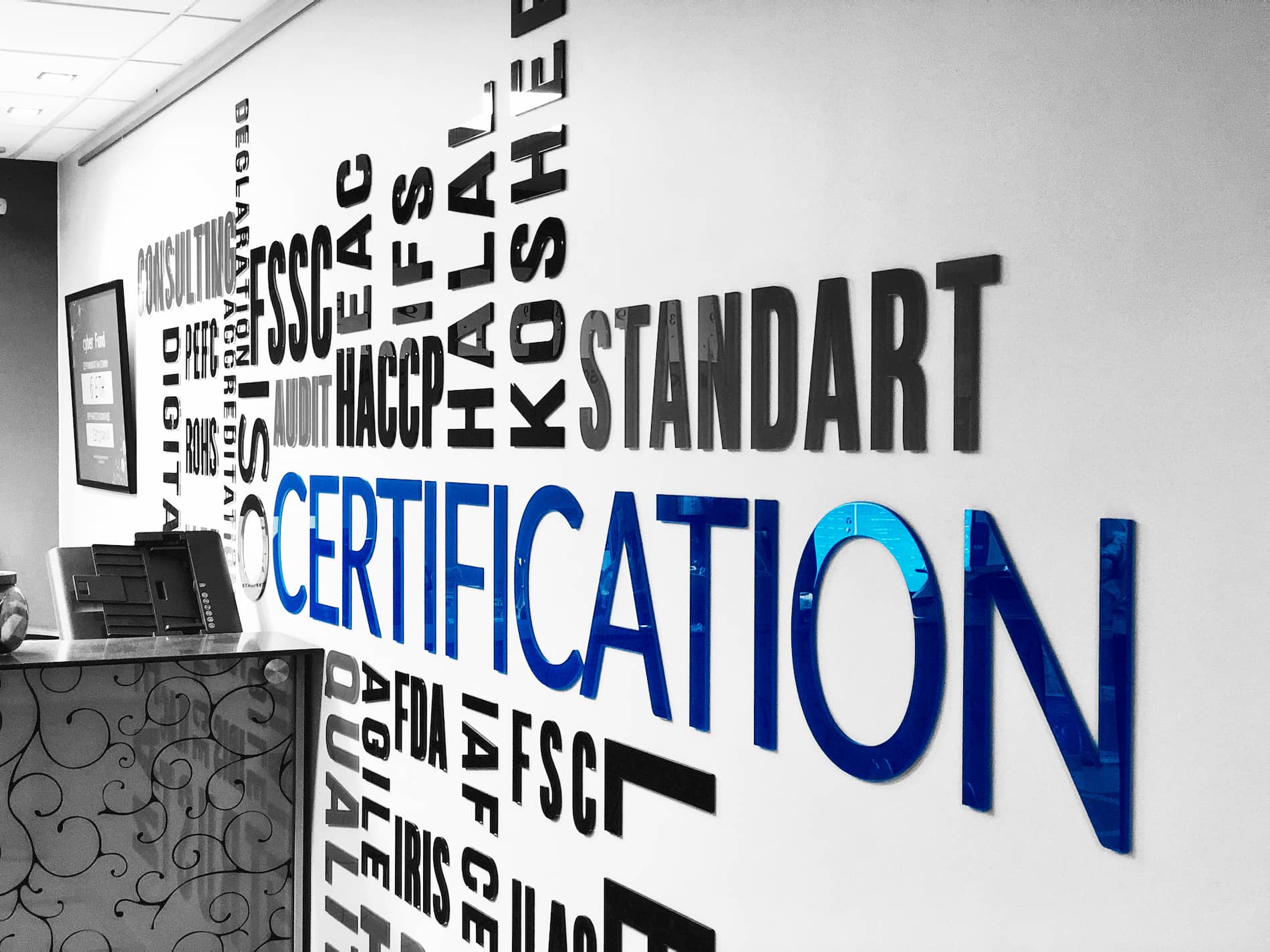 Стена в офисе Easy Standart с синими объёмными буквами CERTIFICATION, чёрными STANDART и названиями ISO, HACCP, HALAL, KOSHER, FSSC, FDA